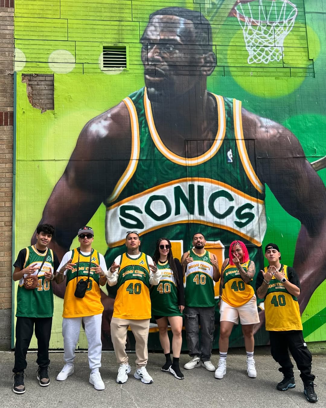 Community members wearing Shawn Kemp jerseys celebrating in front of his Seattle SuperSonics mural